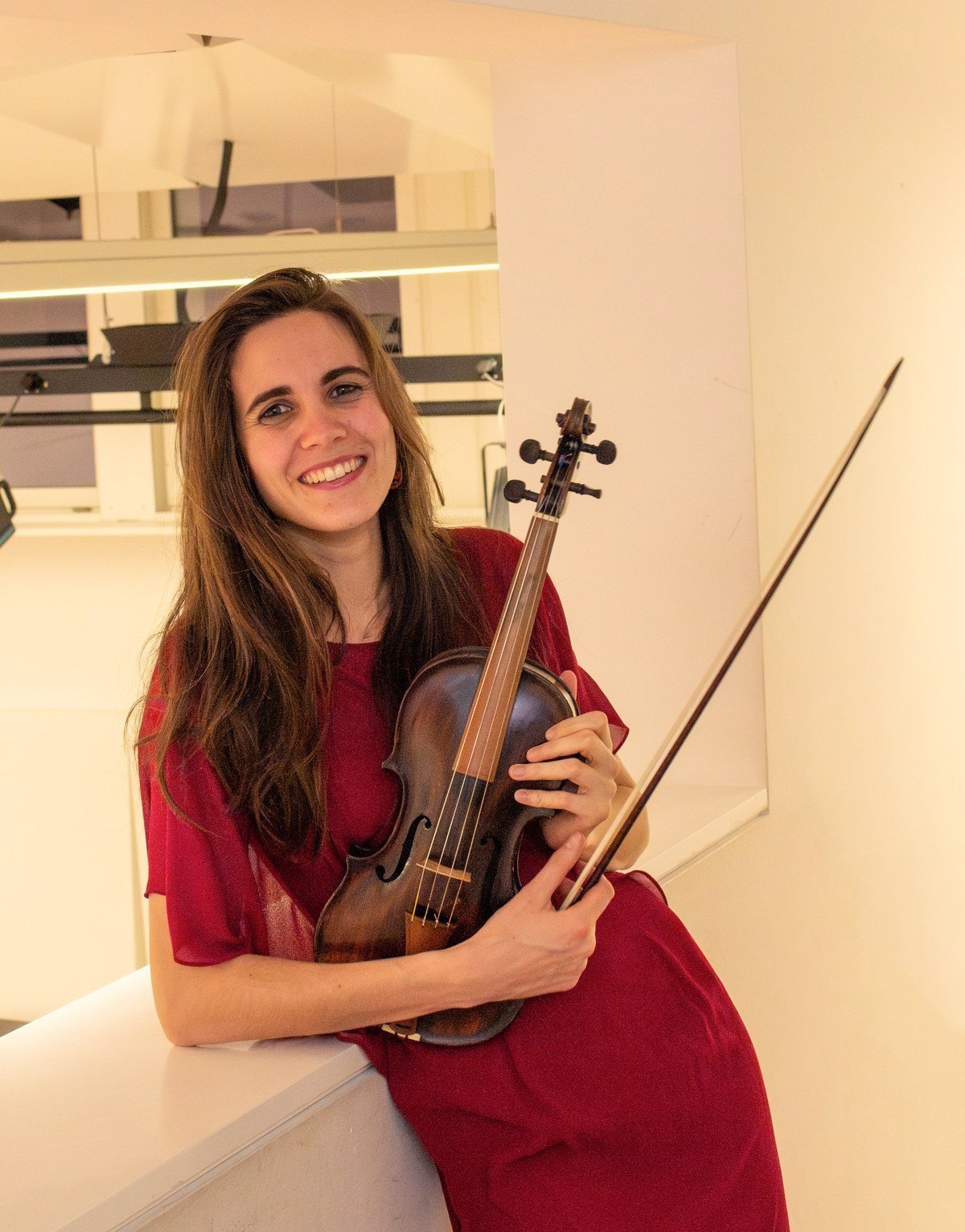 Rahel Boell im roten Kleid mit Geige, an eine Brüstung gelehnt